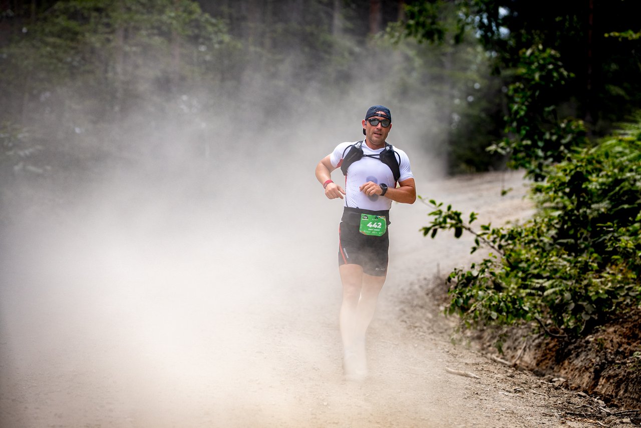 A determined athlete runs through a dusty trail in a lush forest during a marathon in Sapanca, Türkiye.
